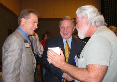 John showing Roger Worthington (l) and Senator Dick Durbin recent photographs of him climbing a mountain in Hawaii, post-surgery at the 2006 MARF Symposium in Chicago, Illinois held in October, 2006